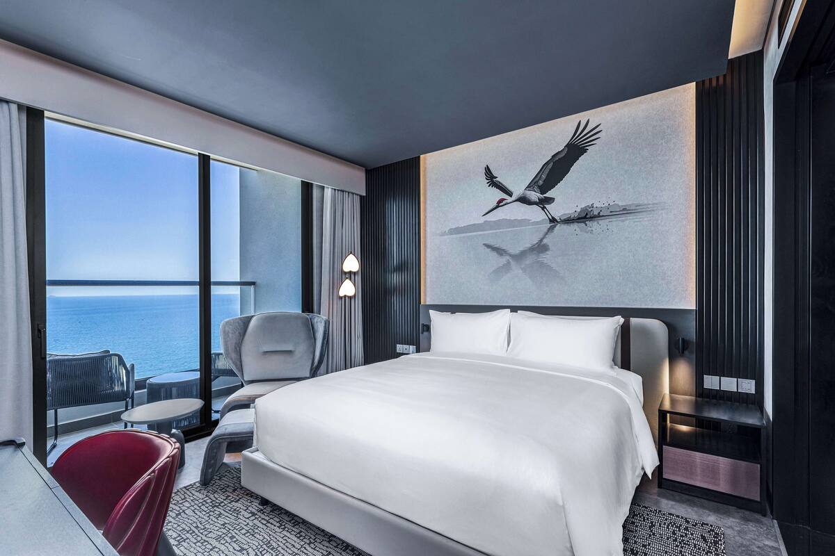 Ein modernes Hotelzimmer mit einem großen Bett, Meerblick, einer Essecke und einem Vogelgemälde.
