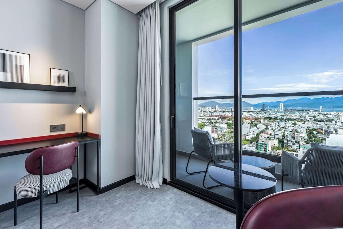 Ein modernes Hotelzimmer mit großem Fenster, Schreibtisch, Stuhl und Essecke mit Tisch und Stühlen.