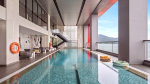 An indoor swimming pool with tiled flooring, a staircase, and lounge chairs. - Radisson RED Danang (Da Nang)