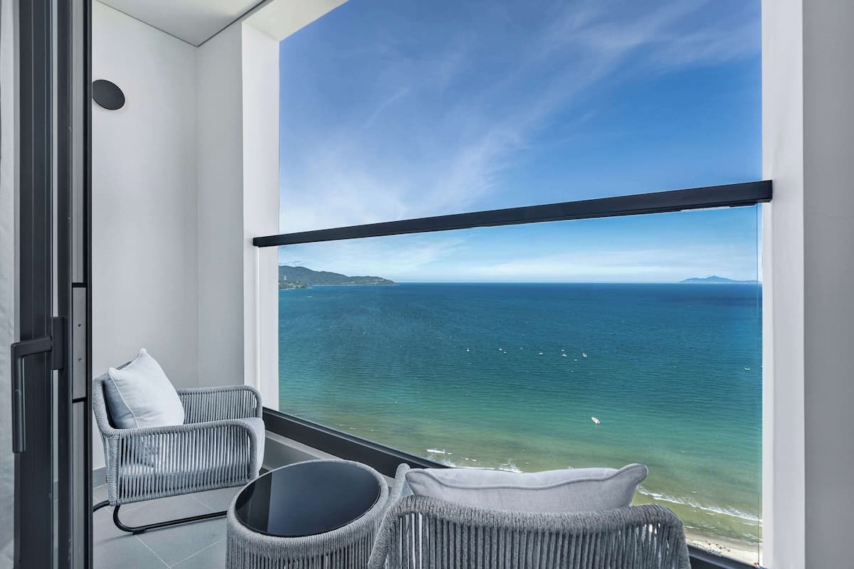 Ein Balkon mit Meerblick, zwei Korbstühle und eine Glastür.