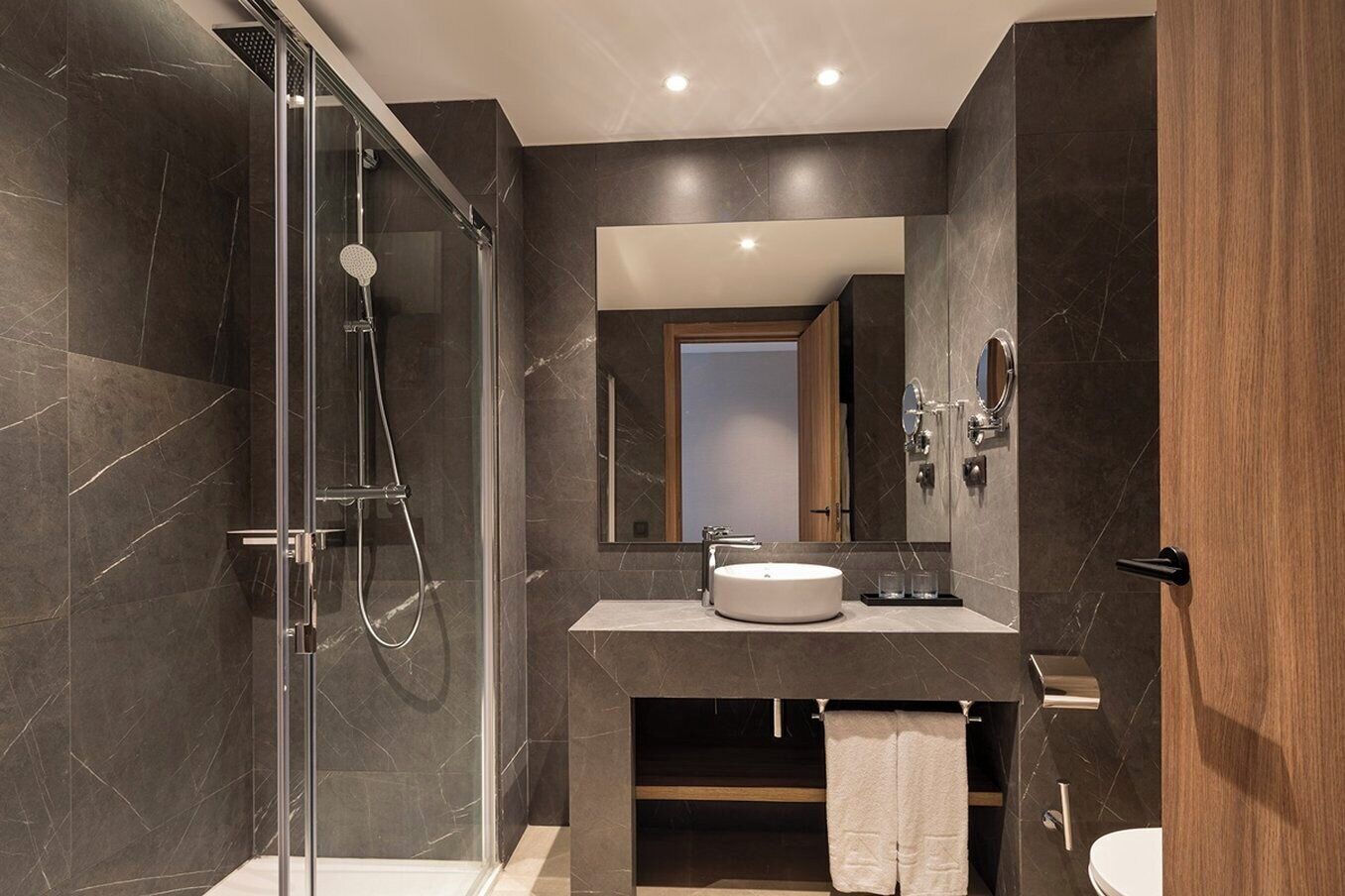 A modern bathroom with a glass-enclosed shower, a round sink, and a large mirror.