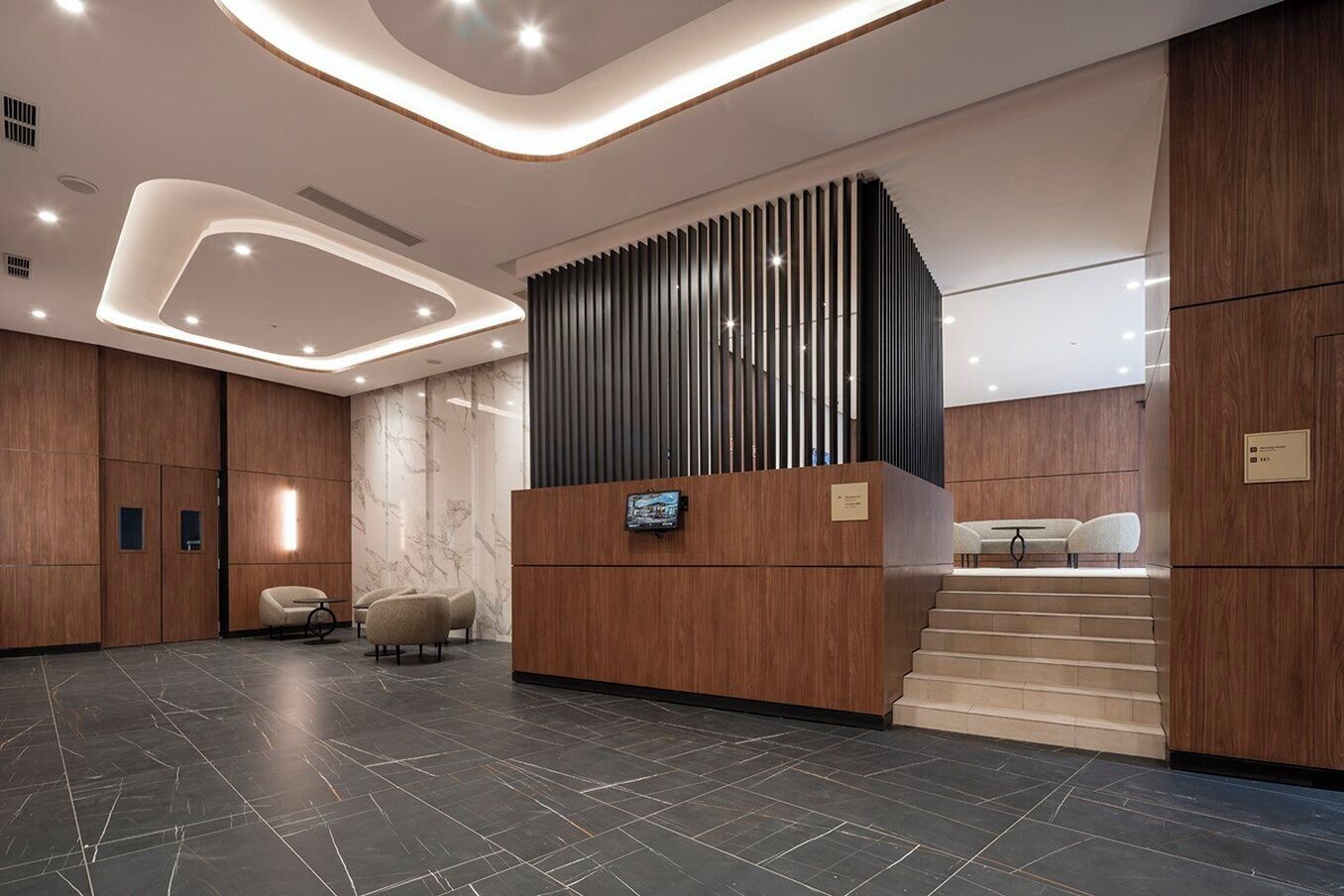 Un área de recepción moderna con un mostrador de madera, un espacio de espera con sillas y una escalera.