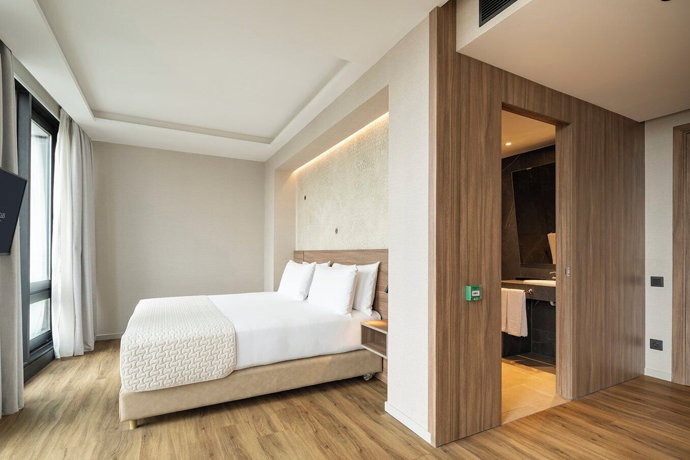 Ein modernes Hotelzimmer mit einem großen Bett, Holzböden, einem eingebauten Kleiderschrank und einem durch eine geöffnete Tür einsehbaren Badezimmer.