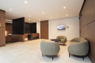 A modern lobby with a reception desk, two armchairs, a small table, and a television on the wall.