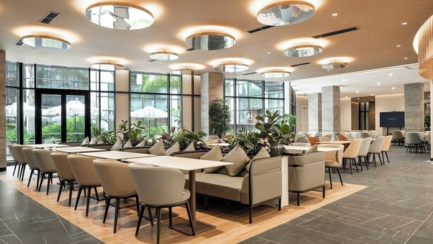Un espace repas moderne avec des tables rondes, des sièges confortables et de grandes fenêtres offrant une vue sur l’extérieur.