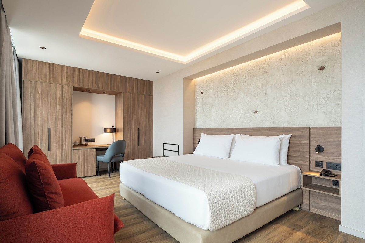 A modern hotel room with a large bed, a desk, and a chair.