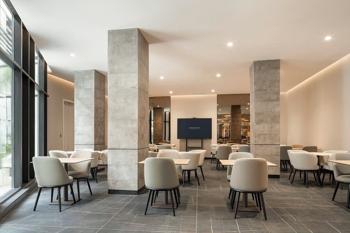 Un restaurant moderne avec de hauts plafonds, de grandes colonnes et un téléviseur à écran plat fixé au mur.