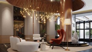 Un hall d’entrée moderne avec un plafond haut, des luminaires suspendus et différents types de sièges, notamment un fauteuil rouge et des fauteuils blancs.