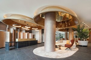 A modern lobby with large cylindrical columns, a reception desk, and a seating area with a potted plant.
