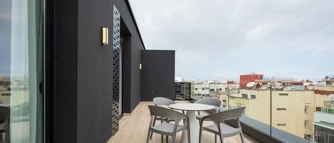 Un balcón con mesa y sillas, una pared oscura y vista a la ciudad.