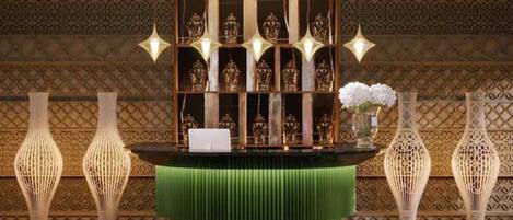 A reception desk with a green cushioned top, surrounded by decorative vases and a patterned wall.
