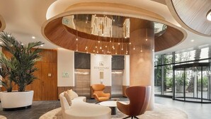 Un hall d’hôtel moderne avec un espace salon central, un comptoir d’accueil et une grande plante en pot.