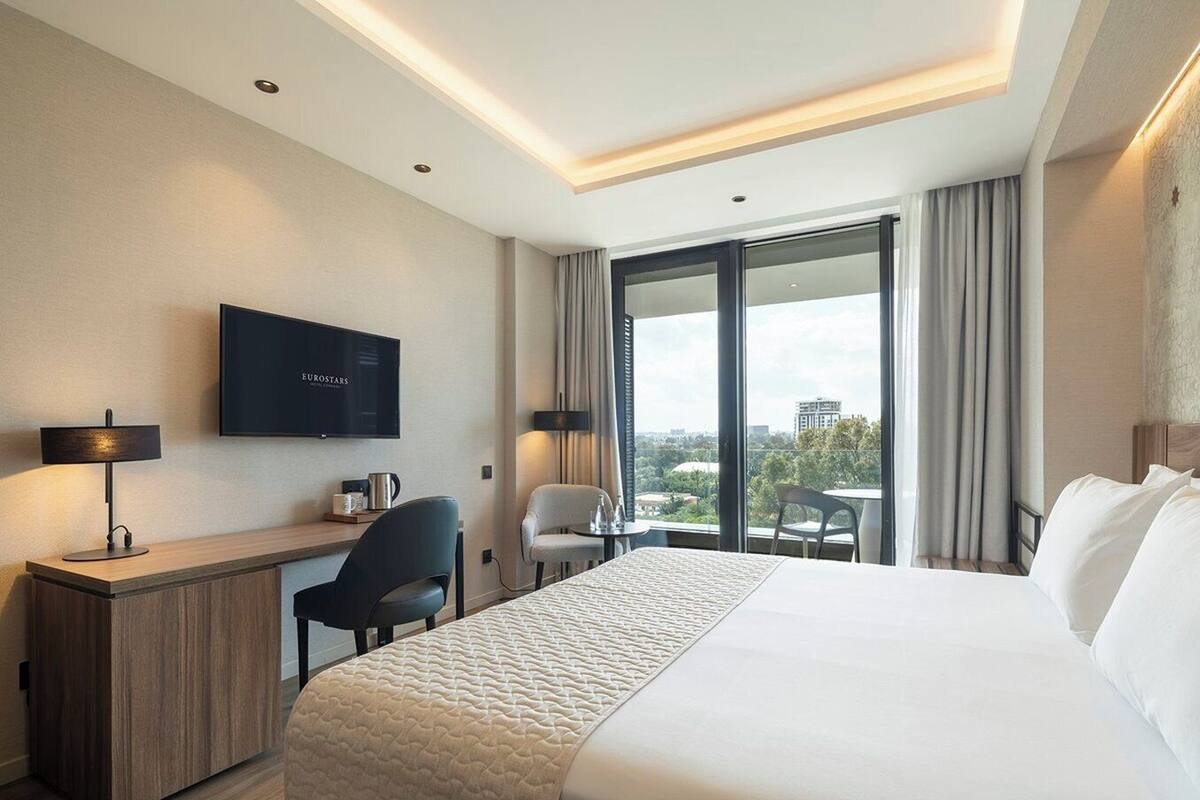 Une chambre d’hôtel avec un grand lit, un bureau avec une chaise, une télévision et une vue sur la ville.