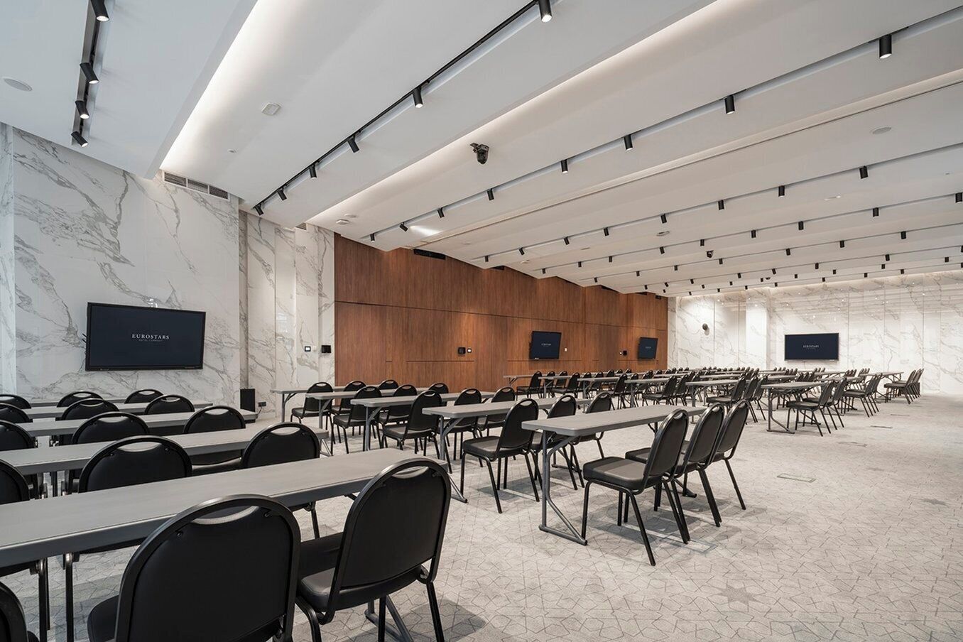 Un salón de conferencias con filas de mesas y sillas, paredes de mármol y una pared decorativa de paneles de madera.