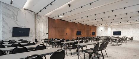 Un salón de conferencias con filas de mesas y sillas, paredes de mármol y una pared decorativa de paneles de madera.