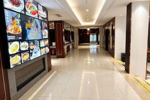 Ein Hotelgang mit Fliesenboden, einer Wand mit digitalen Menütafeln und einer Holztür am Ende.
