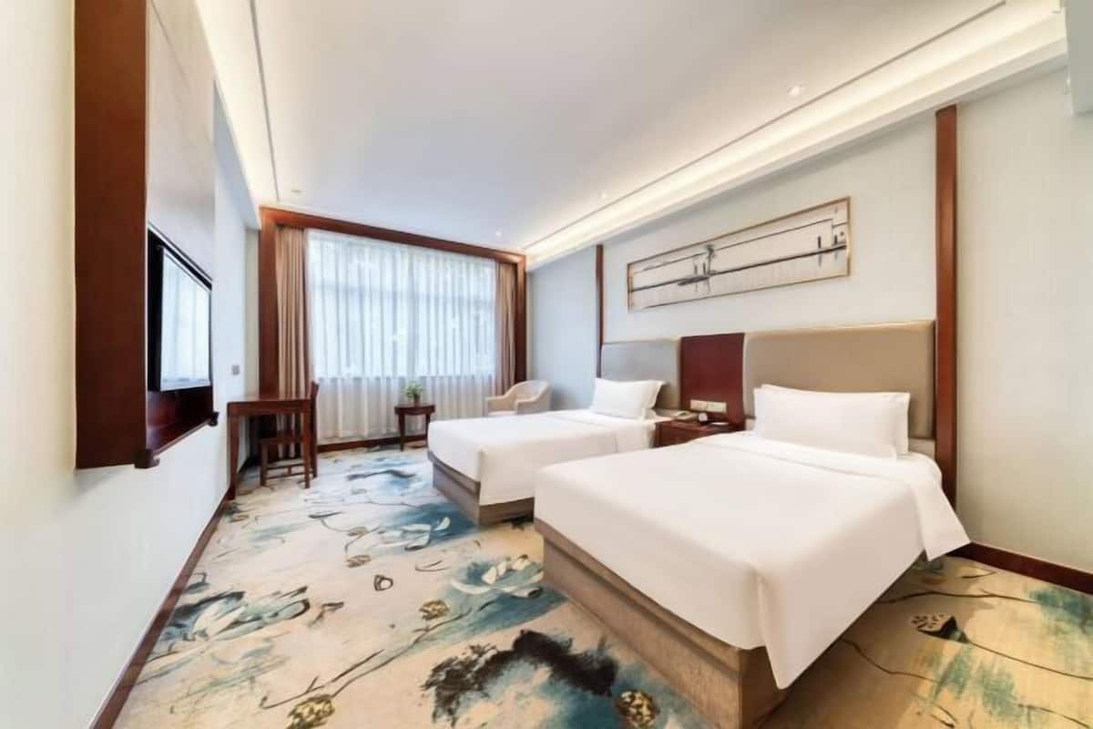 Une chambre d’hôtel avec deux lits, un bureau, une chaise et une grande fenêtre avec des rideaux.