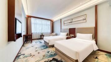 Quarto de hotel com duas camas, uma escrivaninha, uma cadeira e uma janela grande com cortinas.