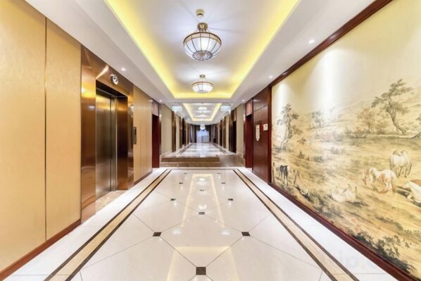 A hotel corridor with a long hallway, elevators, and a mural on the wall.