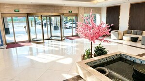 A hotel lobby with a reception desk, a glass door entrance, a small indoor garden with pink flowers, and a seating area with sofas. - Hangzhou Huaxi Hotel (Yintai Department Store Linping Branch) (Hangzhou)