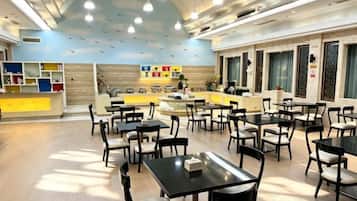 A spacious indoor dining area with multiple tables and chairs, a counter with a display, and a wall with shelves.