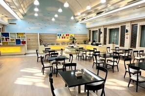 Un grand espace de restauration intérieur, doté de nombreuses tables et chaises, d’un comptoir avec présentoir et d’un mur avec des étagères.
