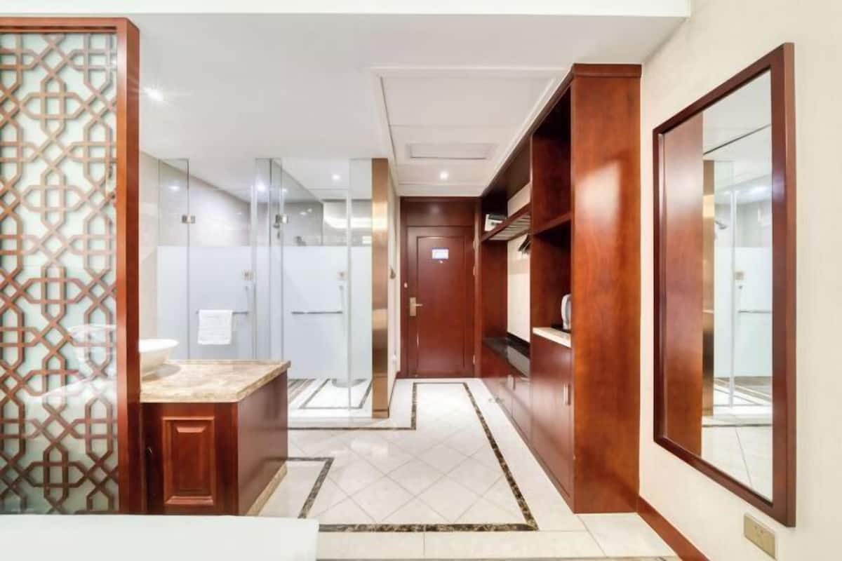 Une salle de bain d’hôtel moderne avec une douche en verre, un meuble-lavabo en bois et un grand miroir.