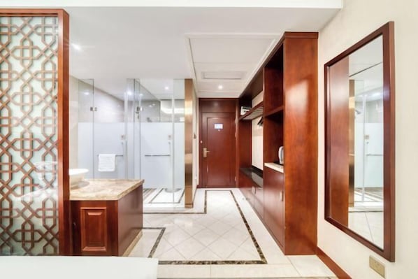 Un bagno d'hotel moderno con cabina doccia in vetro, un mobile lavabo in legno e uno specchio grande.