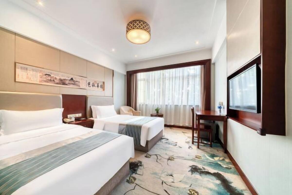 Une chambre d’hôtel avec deux lits, un bureau, une télévision et une grande fenêtre avec des rideaux.