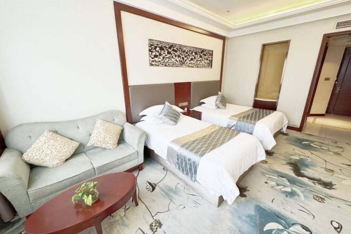Une chambre d’hôtel avec deux lits, un canapé, une table basse et une œuvre d’art accrochée au mur.