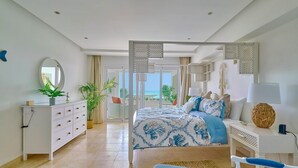 Een slaapkamer met een bed, een dressoir, een bureau en uitzicht op zee.