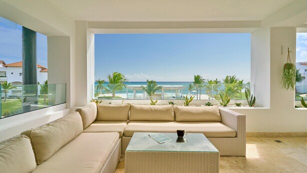 Een moderne woonkamer met een groot raam dat uitkijkt over een strand en een zwembad.