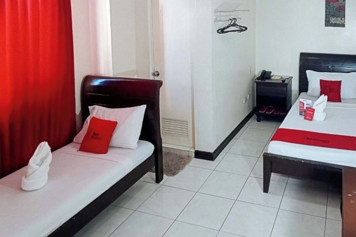 Una habitación de hotel con dos camas, una mesita de noche y una cortina roja.
