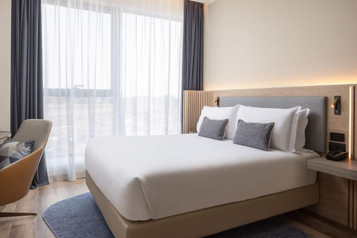 A hotel room with a large bed, a bedside table with a phone, and a chair.