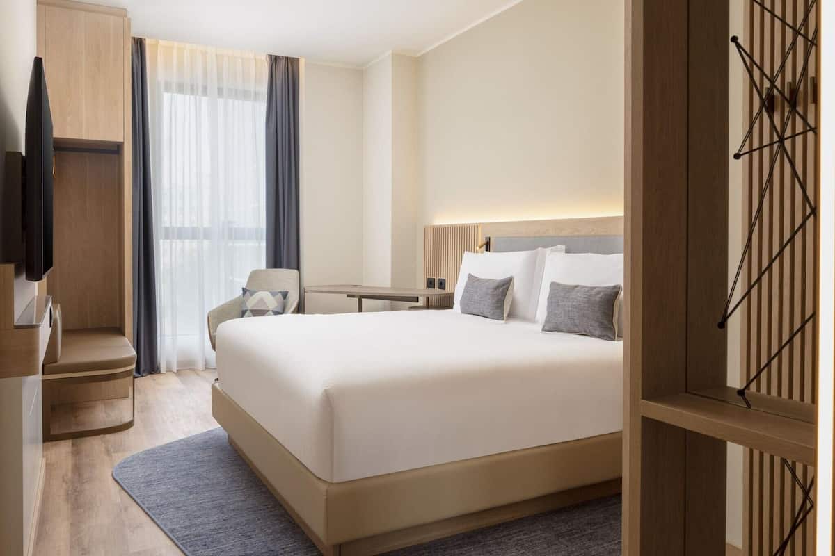 A hotel room with a large bed, a desk, a chair, and a TV.