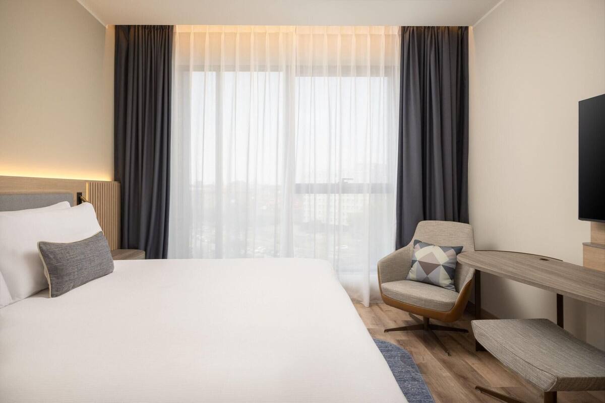 A hotel room with a large bed, a chair, a desk, and a TV.