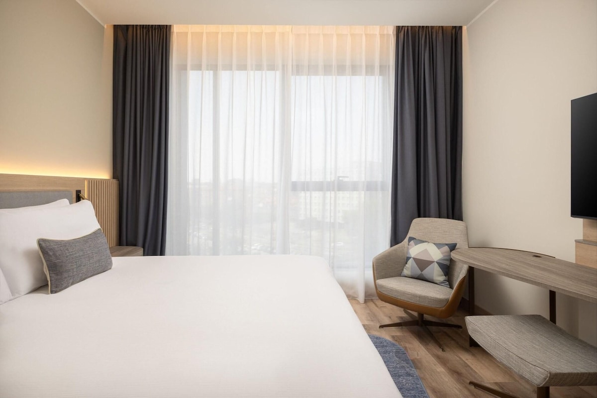 A hotel room with a large bed, a chair, a desk, and a TV.