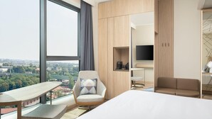 Une chambre d’hôtel moderne dotée d’une grande fenêtre, d’un lit, d’un bureau, d’une chaise, d’un canapé et d’une télévision.