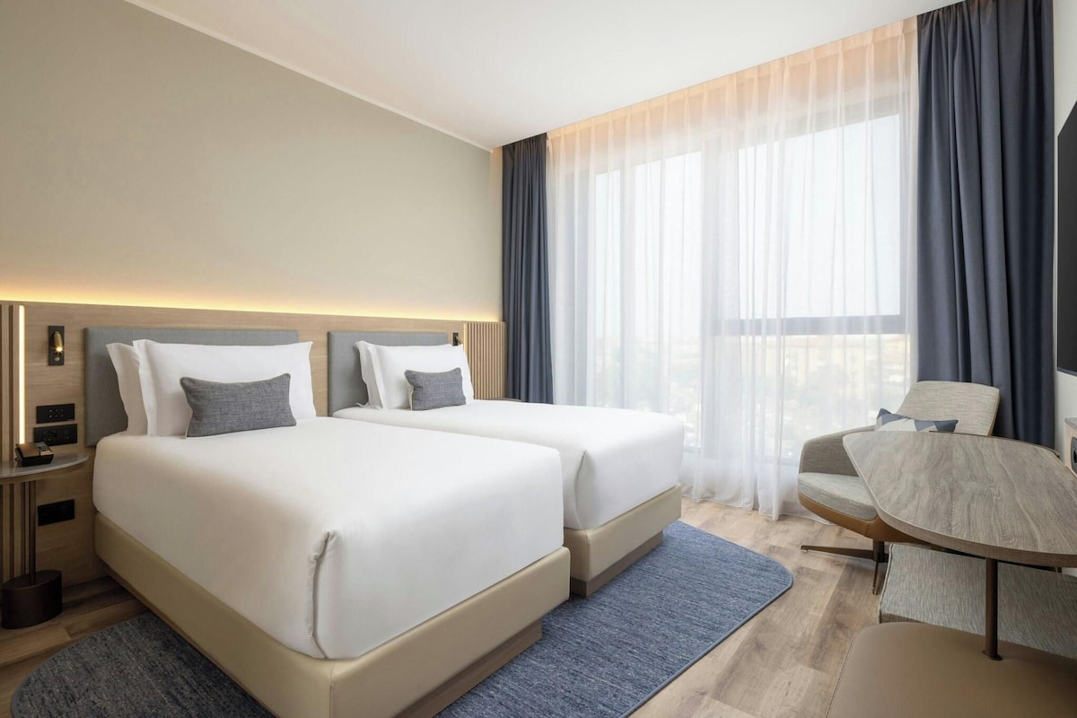 A modern hotel room with two beds, a desk, and a chair.