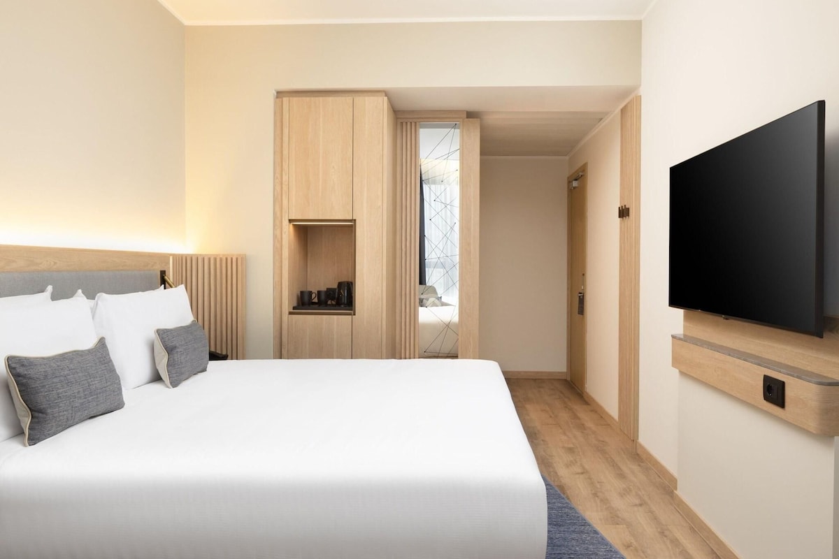 A modern hotel room with a large bed, a TV mounted on the wall, and a wooden wardrobe.
