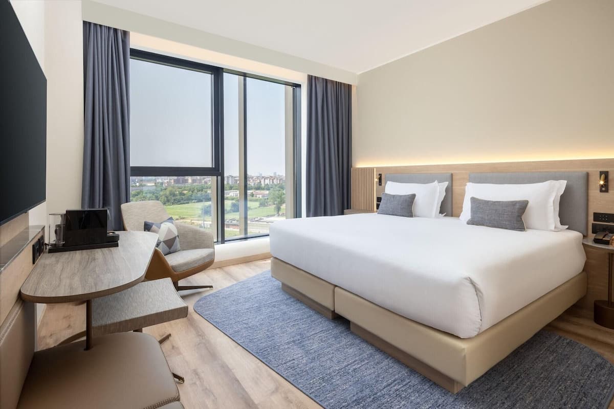 A modern hotel room with a large bed, a desk, and a view of the city.