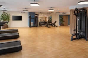 A gym with exercise equipment, wooden flooring, and ceiling lights. - Courtyard Milano Linate (Milan)