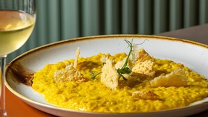 A plate of yellow risotto garnished with croutons and herbs, accompanied by a glass of white wine. - Courtyard Milano Linate (Milan)