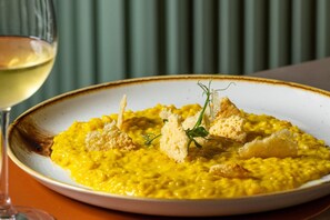 A plate of yellow risotto garnished with croutons and herbs, accompanied by a glass of white wine. - Courtyard Milano Linate (Milan)
