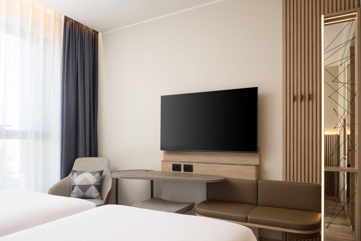 A hotel room with a bed, a sofa, a TV mounted on the wall, and a small table.