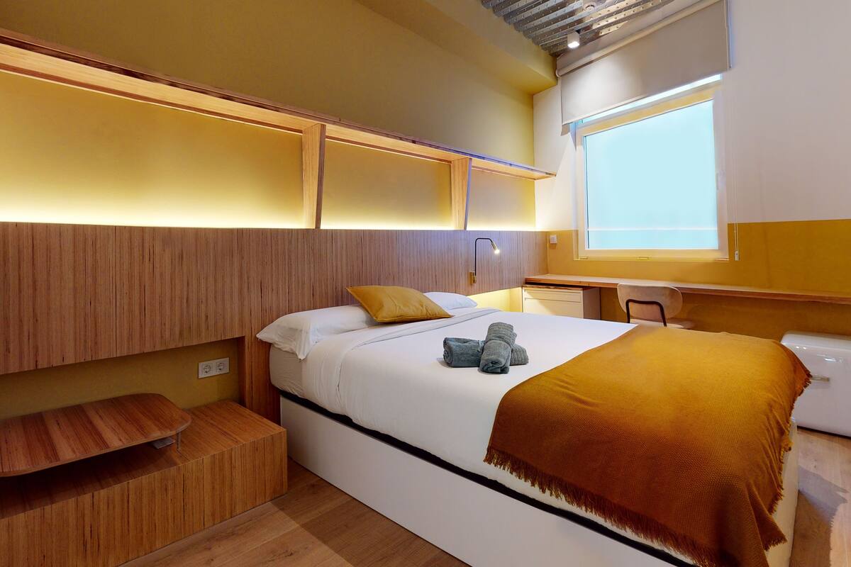 Une chambre d’hôtel de taille réduite, comprenant un lit, une table de chevet et un petit coin salon.