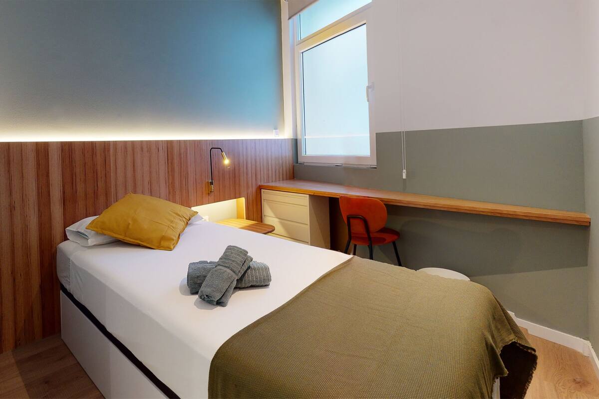 Une chambre à coucher de taille réduite, comprenant un lit, un bureau et une chaise.
