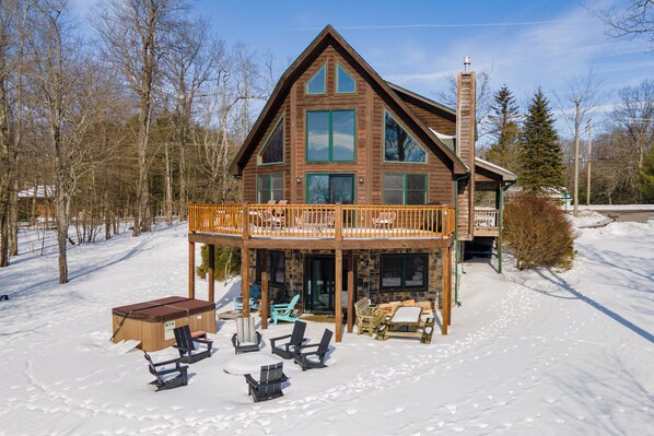 Une cabane en rondins dotée d’un balcon, d’un espace extérieur aménagé et surplombant un paysage enneigé.