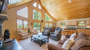 A spacious living area with a high ceiling, large windows, and a kitchen area. - Scenic Retreat w/ Pool Table & Lake Views (Swanton)