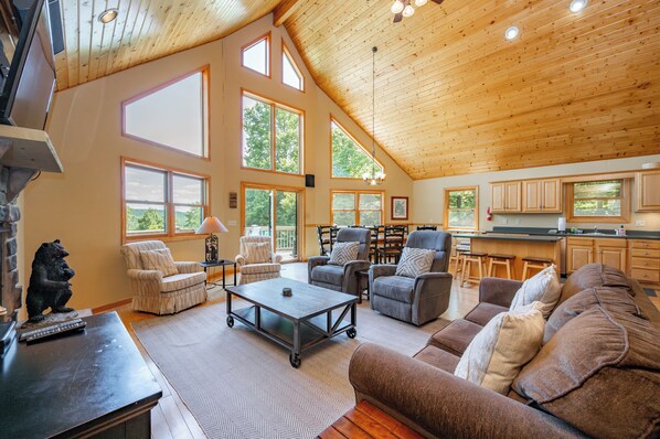 A spacious living area with a high ceiling, large windows, and a kitchen area. - Scenic Retreat w/ Pool Table & Lake Views (Swanton)